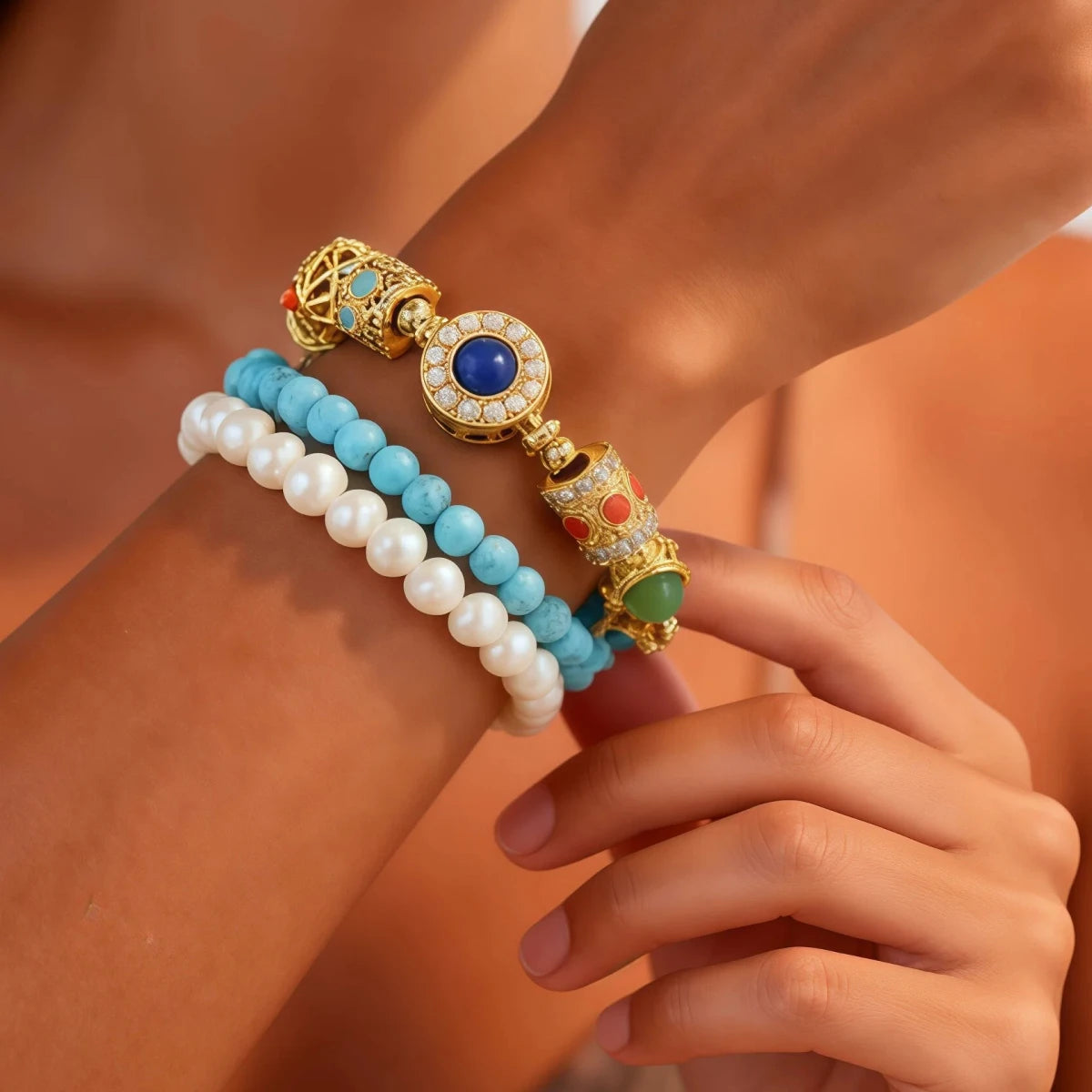 A woman's wrist wearing the Triple Celestial Flow Bracelet. The image shows the layered look of pearls and turquoise beads with a central Lapis Lazuli gold charm, demonstrating its elegant and bohemian style.