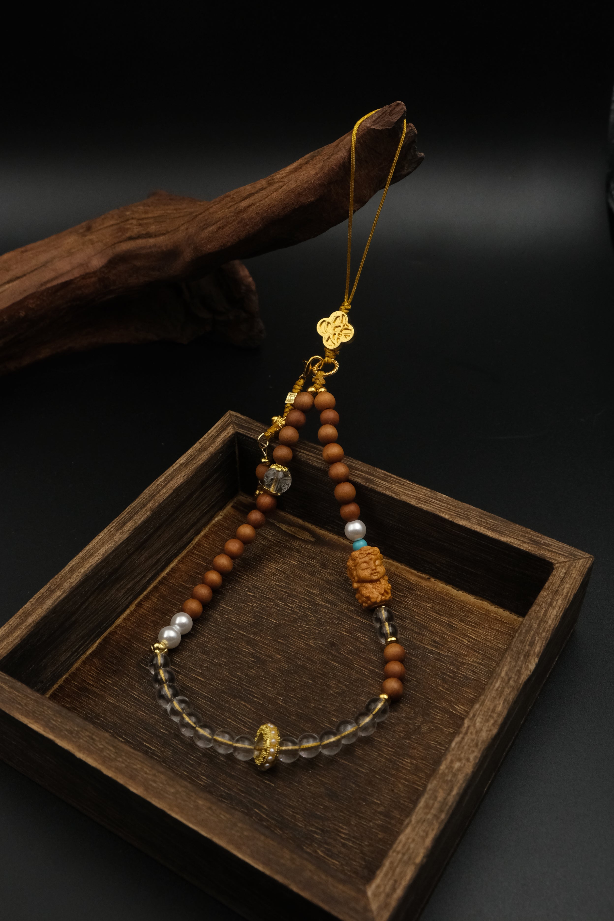Calm & Positivity – Sandalwood Buddha Charm with gold accents on a wooden tray against a dark background