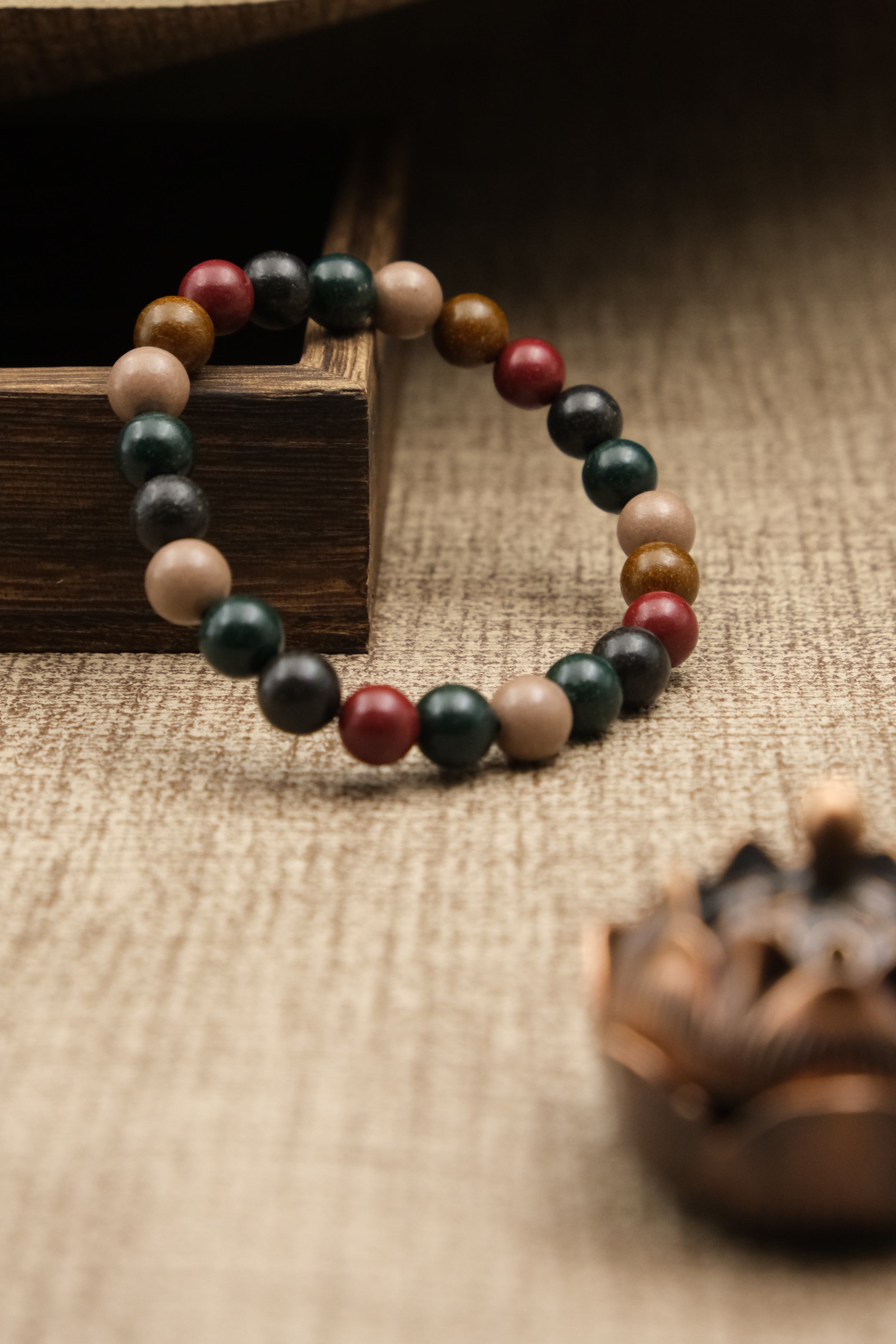 Multicolored beaded Aromatherapy bracelet on a textured surface with a wooden box and pine cone.