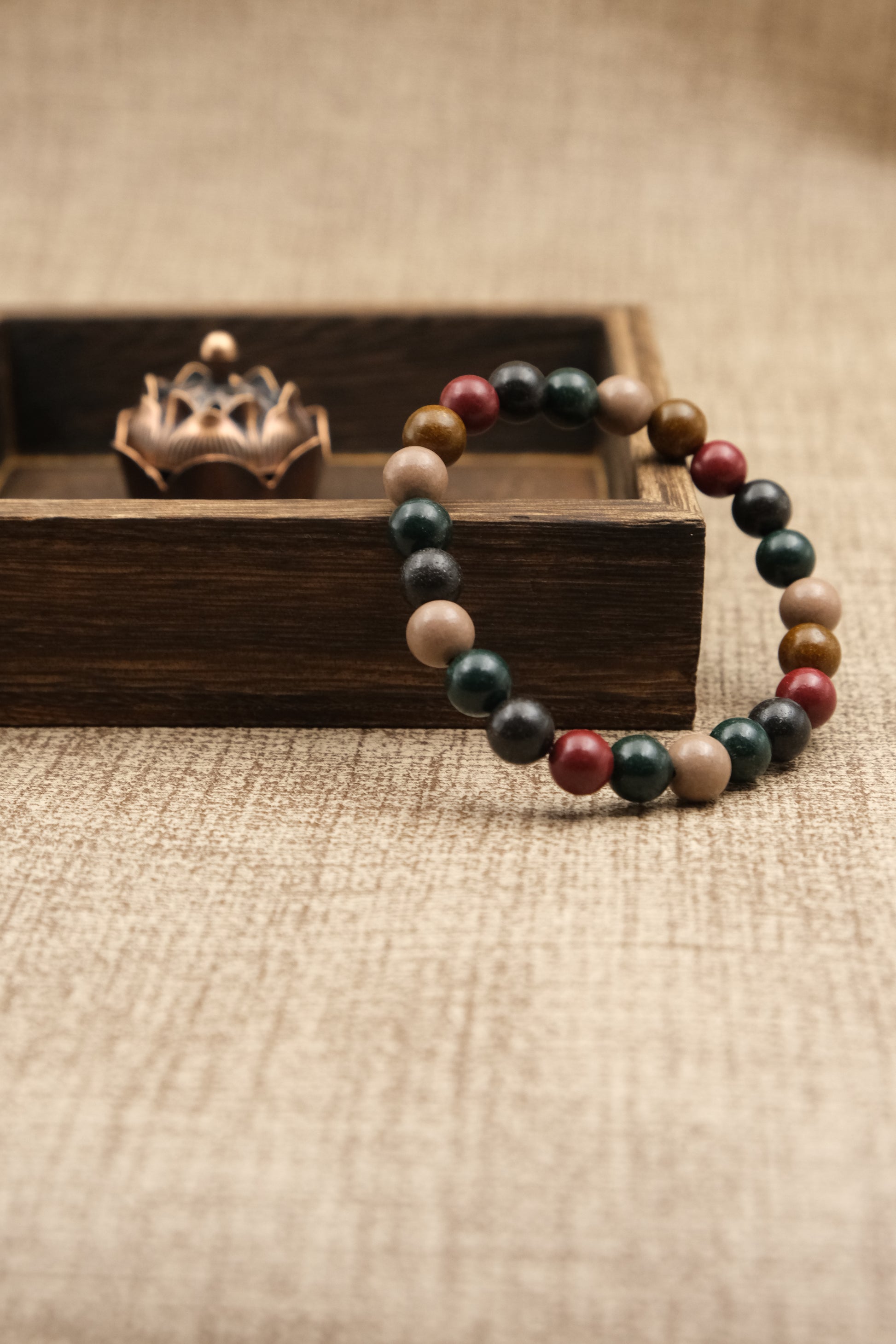 Multicolored beaded Aromatherapy bracelet with five elements on a wooden stand with a textured brown background