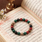 Handmade stretch bracelet with black, red, green, and natural wooden beads displayed on ancient manuscript with brass oil lamp and daisies.