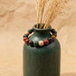 Green ceramic vase with dried grasses and a beaded bracelet on a beige background