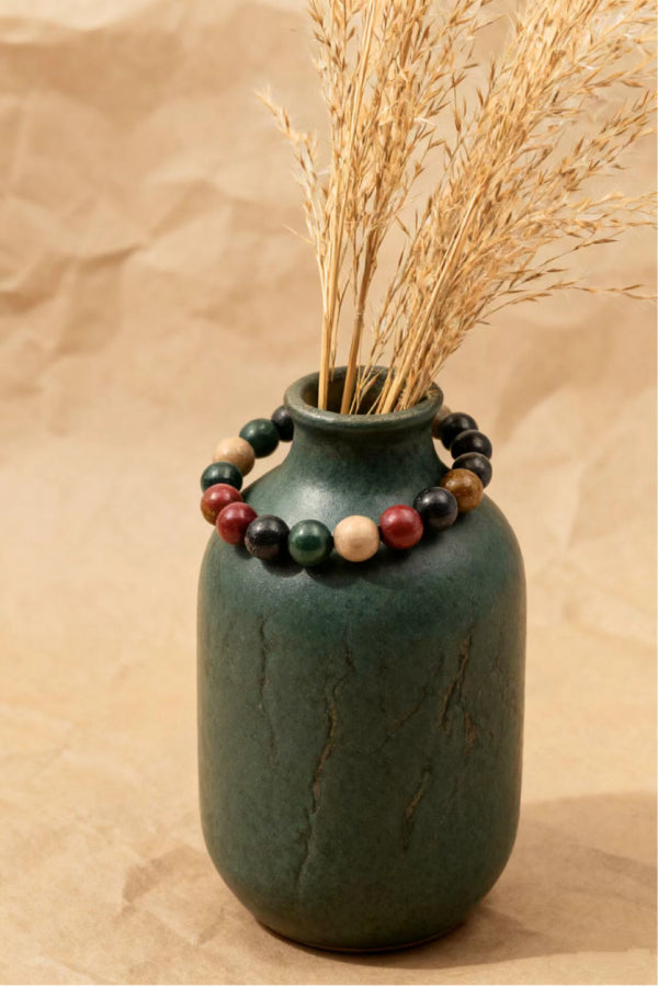 Green ceramic vase with dried grasses and a beaded bracelet on a beige background