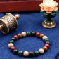 Multicolored beaded bracelet on a blue fabric background with a prayer wheel and lotus flower decoration.