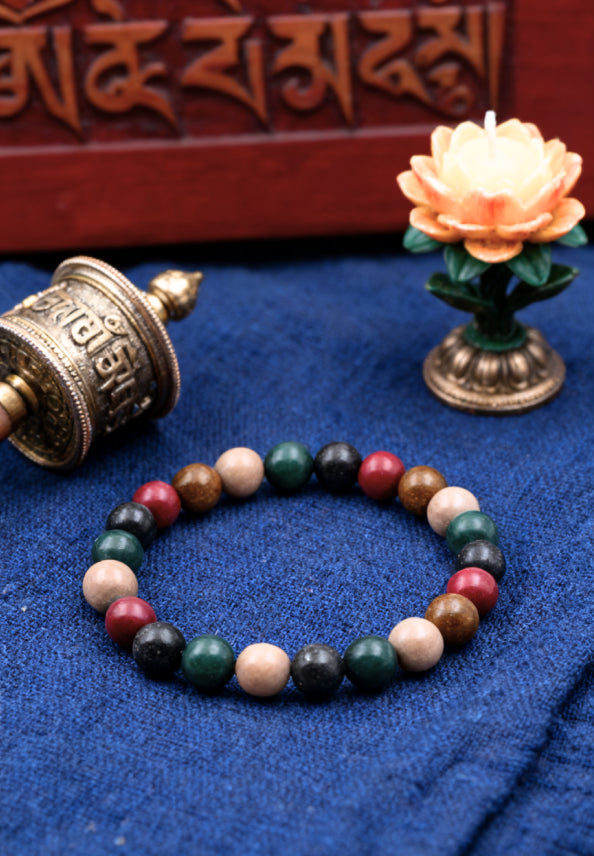 Multicolored beaded bracelet on a blue fabric background with a prayer wheel and lotus flower decoration.