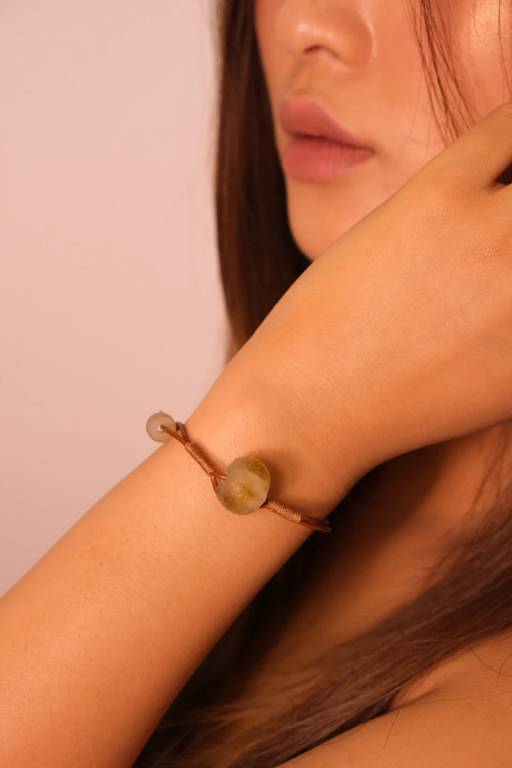 Close-up of a person wearing a bracelet with a stone on a plain background