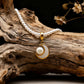 Tibetan Moonlight Pearl Necklace draped over a textured wooden log. The necklace features a strand of small white pearls and a gold-rimmed mother-of-pearl crescent moon pendant cradling a central pearl, accented by dried flowers in the background.