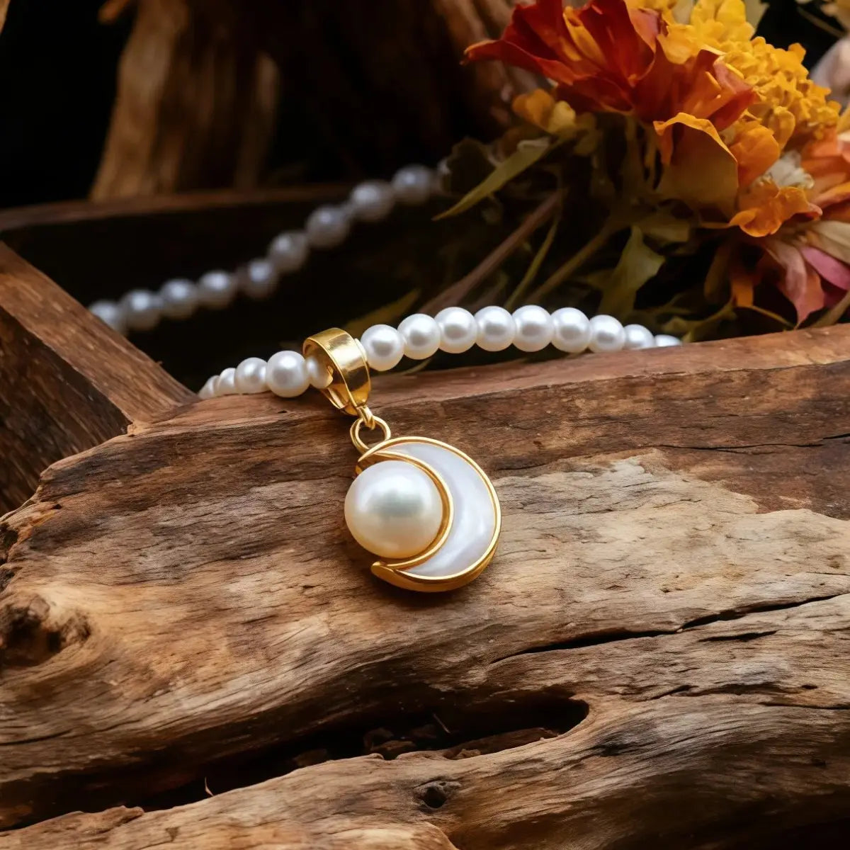 Pearl bracelet with a gold charm on a wooden surface with flowers in the background