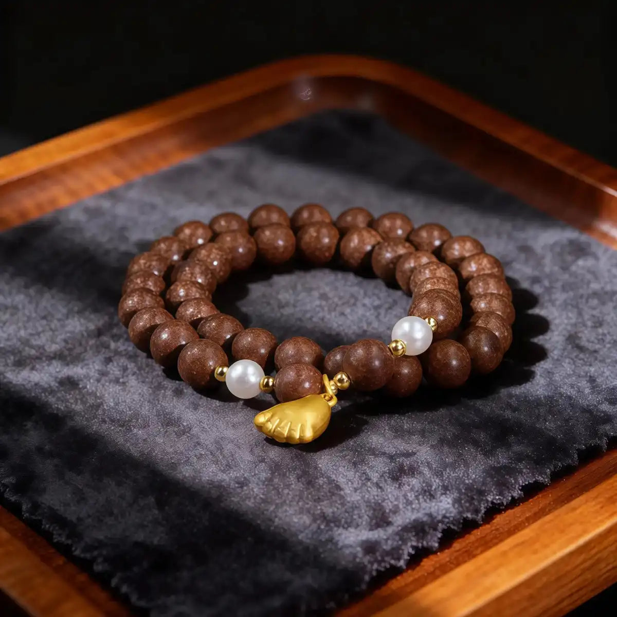 Brown incense beaded bracelet with white pearls and a gold charm on a dark gray fabric background.