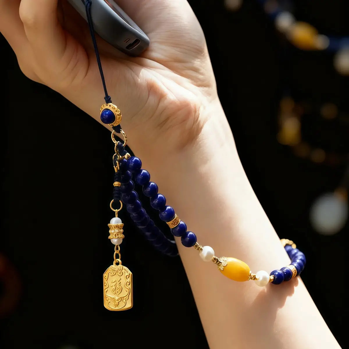 Hand wearing a beaded bracelet with a gold charm against a dark background