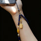 Hand holding a beaded phone charm with blue, gold, and pearl beads against a black background