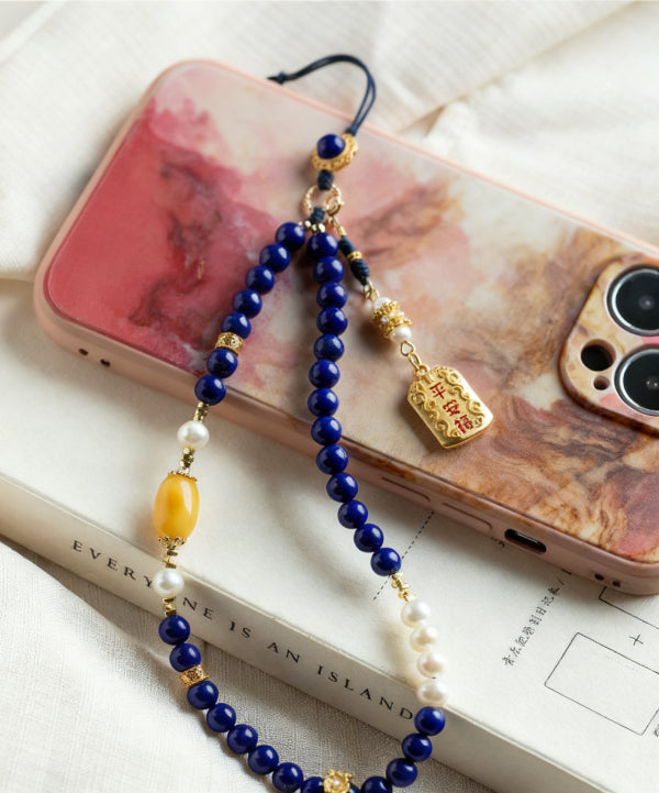 Phone charm with blue beads and a gold tag on a phone case.