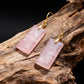 Rose quartz earrings with gold hooks on a wooden surface