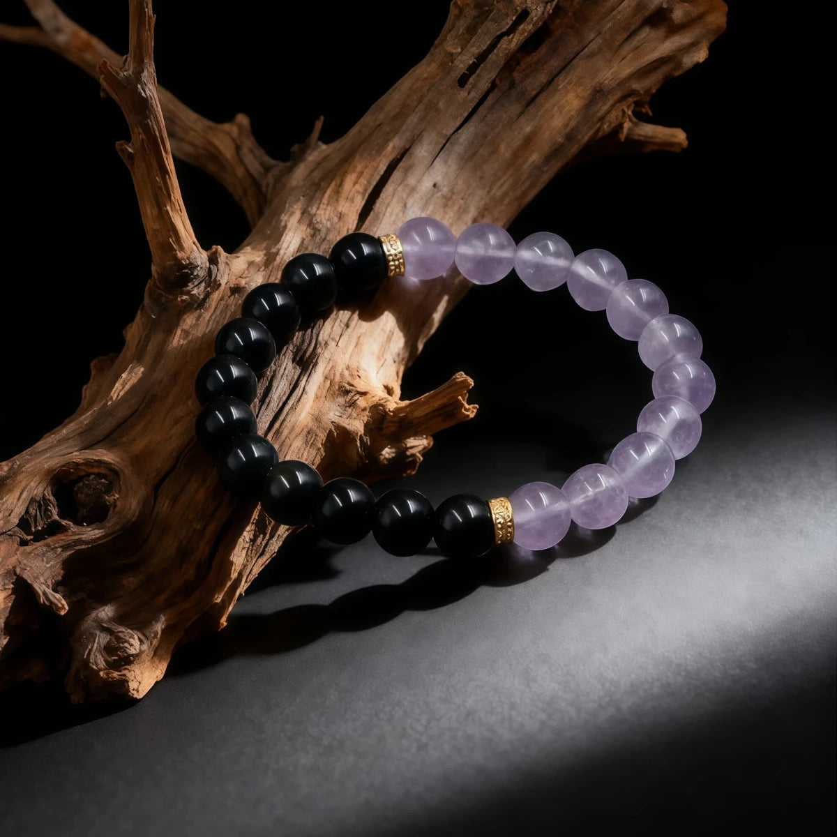 The Tibetan Dual Energy Bracelet draped over a piece of rustic driftwood. The lighting highlights the clarity of the amethyst and the sheen of the black obsidian, evoking a sense of natural healing and spiritual connection.