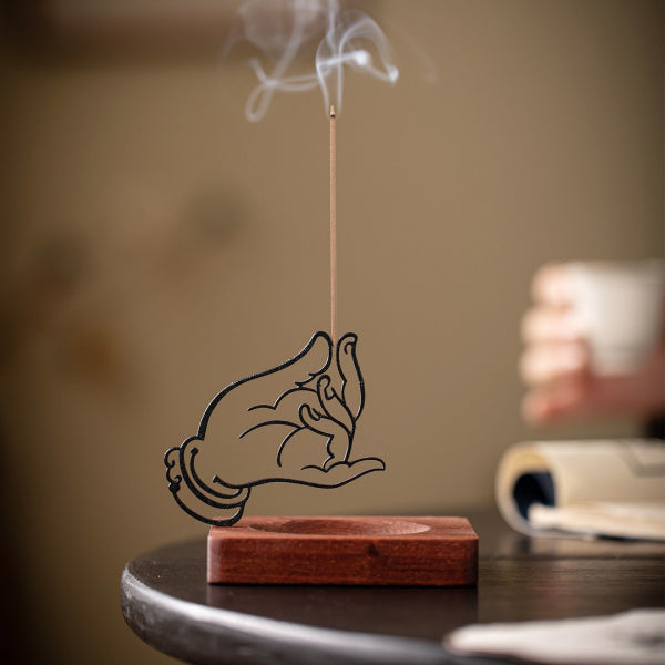 Incense stick with smoke on a wooden holder shaped like a hand holding a heart, blurred background