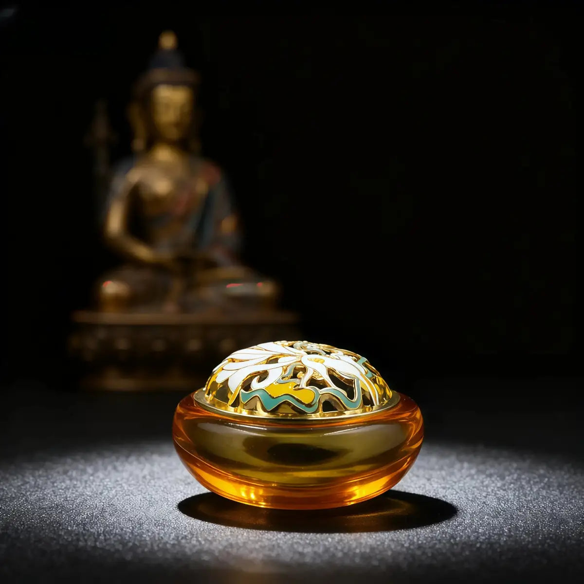 Decorative amber-colored object with intricate design in front of a blurred Buddha statue on a dark background