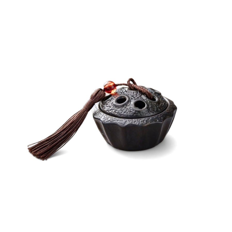 Ceramic lotus pod mini incense burner with dark glaze, lotus-shaped lid, brown tassel, and red bead, symbolizing stillness and clarity.
