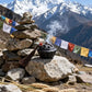 Dark ceramic lotus pod incense burner with tassel and red bead emitting smoke, placed on rocks with snow-capped mountains, prayer flags, and wheat in the background.