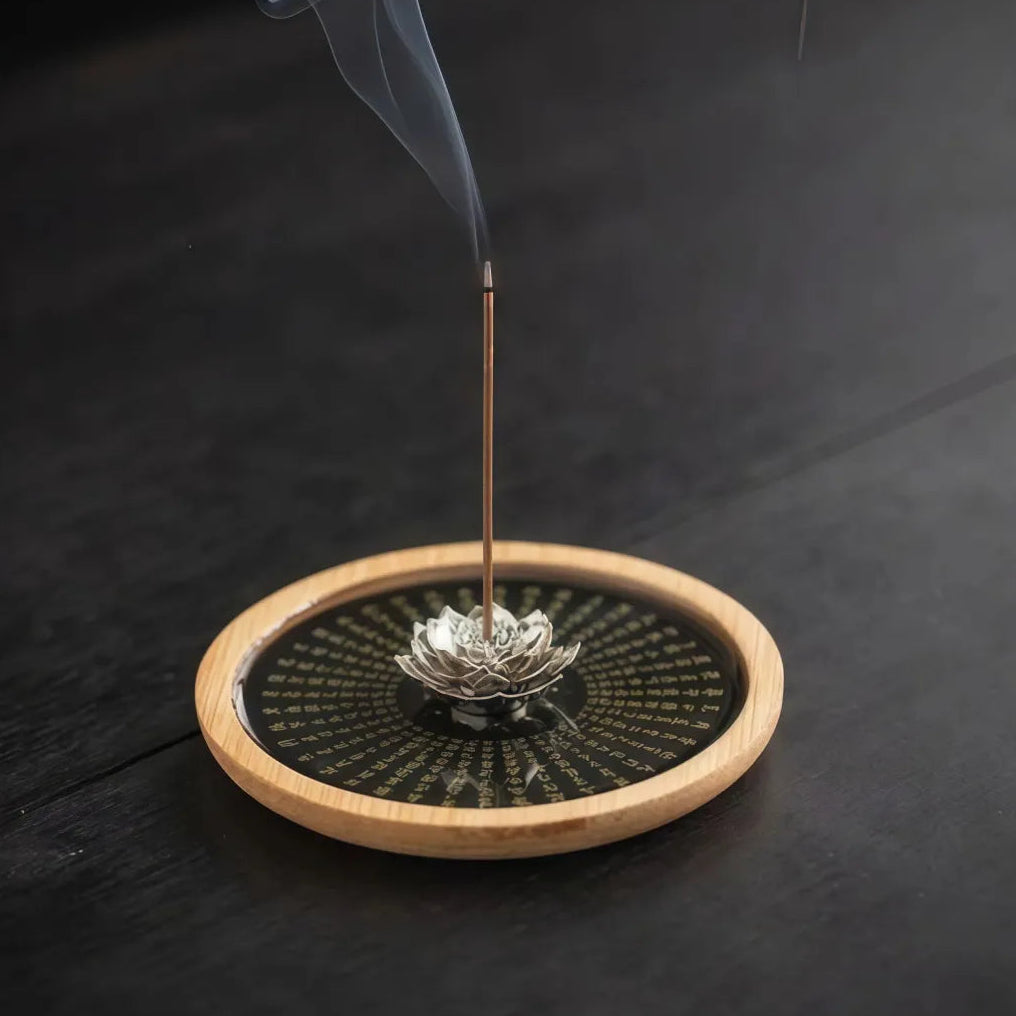 Incense stick with smoke on a wooden coaster with lotus design against a dark background
