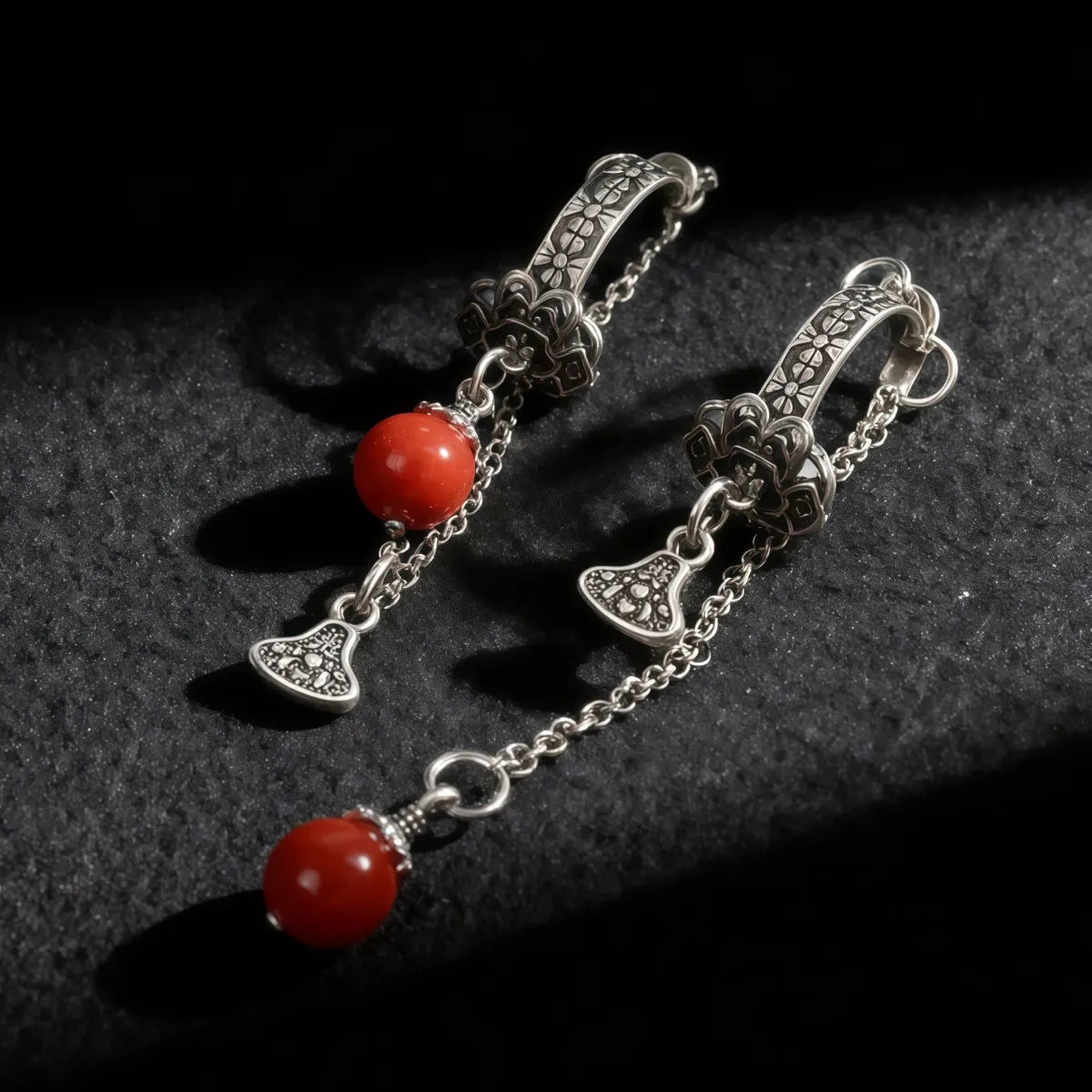 Tibetan Silver earrings with red beads on a dark textured surface