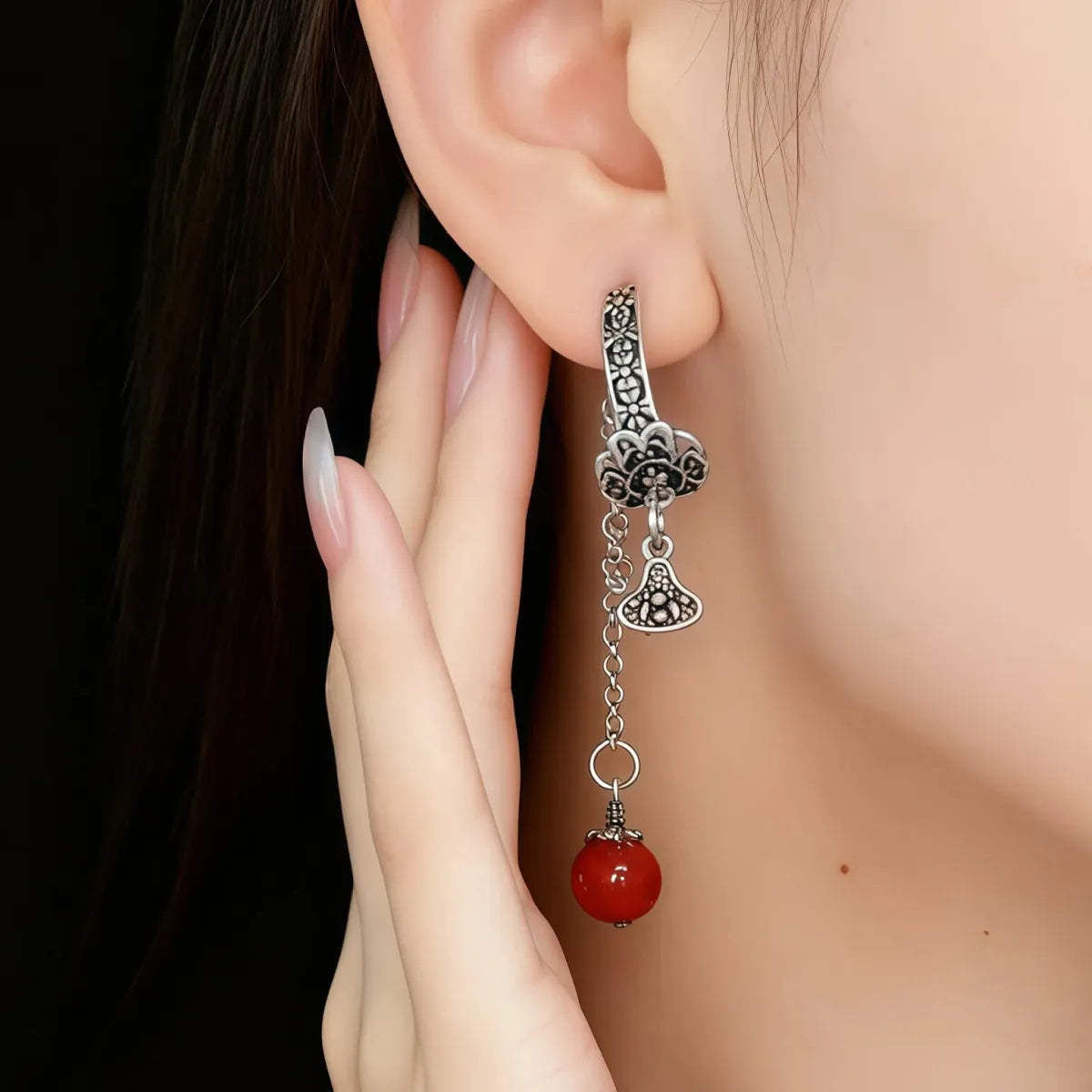 Tibetan silver Earring with red bead and intricate design worn on an ear against a neutral background