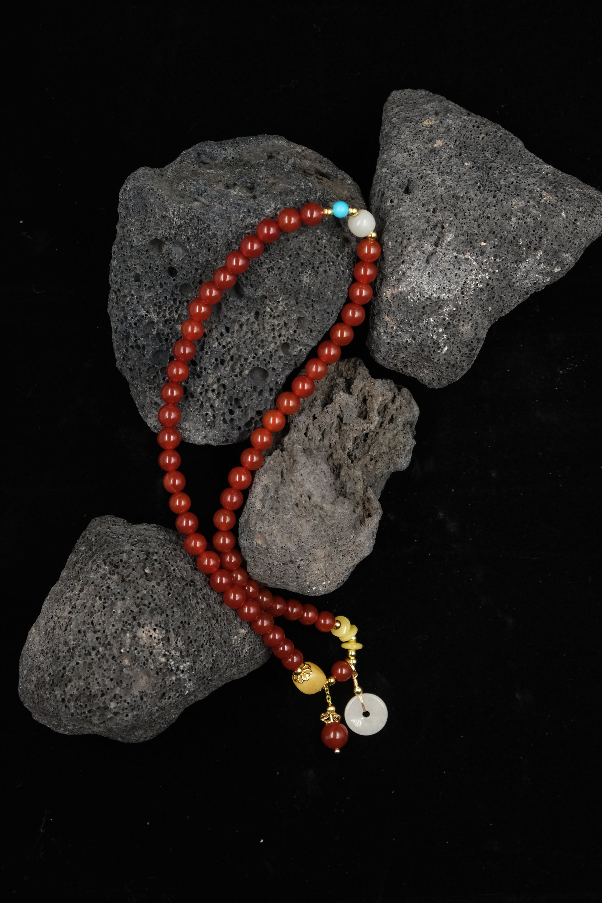 Red beaded Tibetan Blessing Bracelet with colorful accents on dark rocks