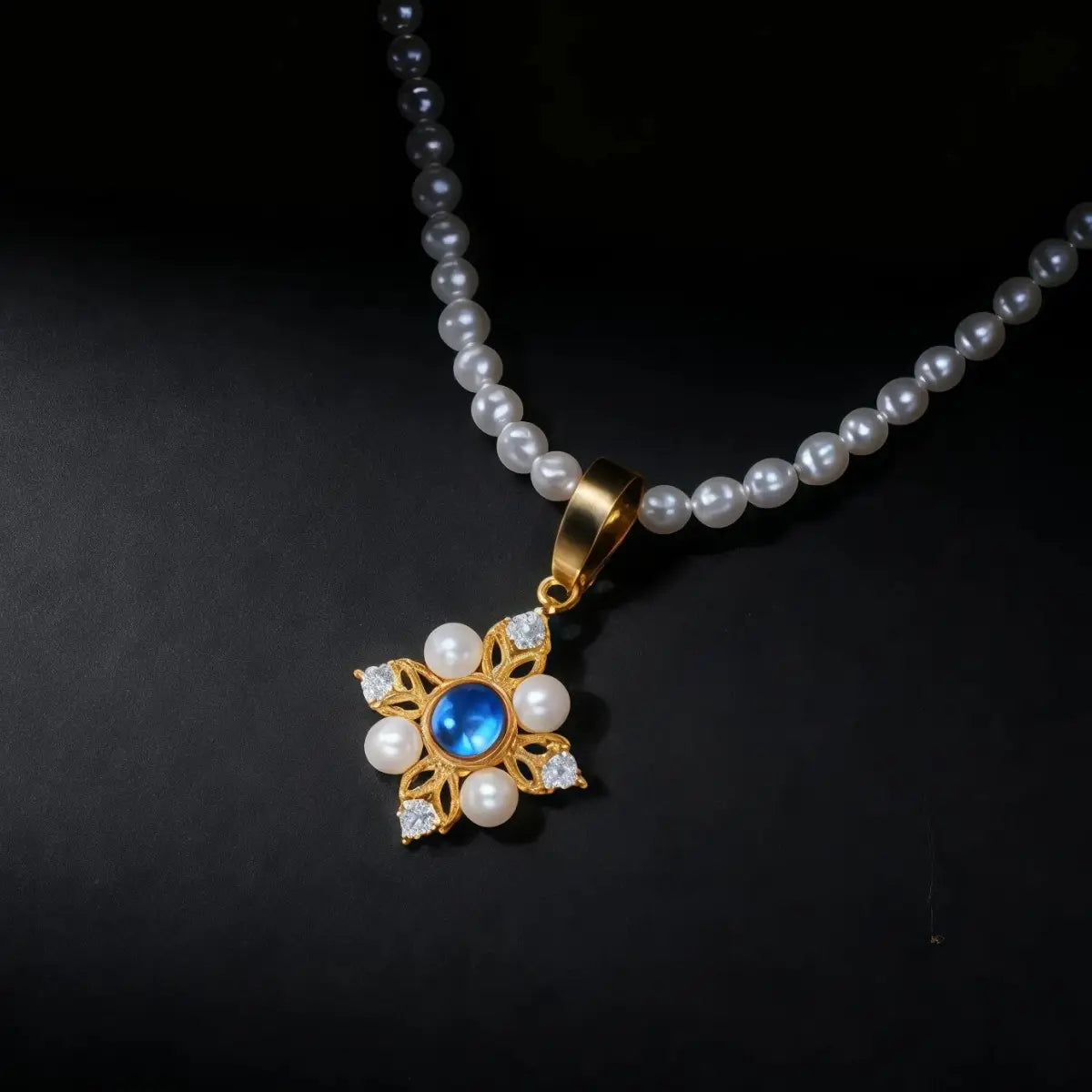 A Tibetan-style pearl necklace featuring a gold floral pendant with a glowing blue moonstone center surrounded by pearls and crystals, symbolizing calm and emotional balance against a dark background.