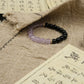 Tibetan Dual Energy,Purple and black beaded bracelet on a textured fabric background with Chinese text