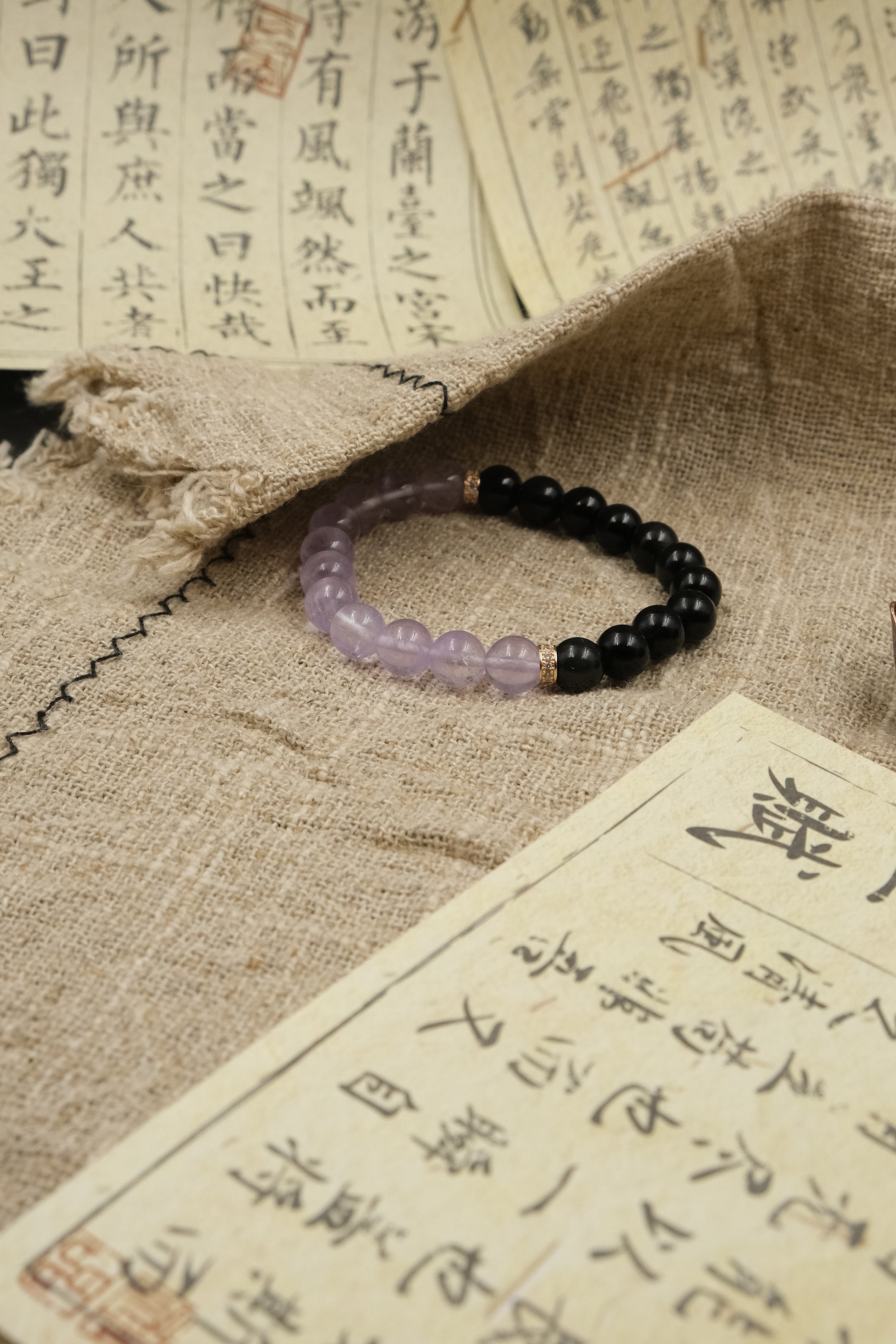Tibetan Dual Energy,Purple and black beaded bracelet on a textured fabric background with Chinese text