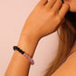 Close-up of a woman wearing the Tibetan Dual Energy Bracelet made of black obsidian and purple amethyst beads, photographed against a light pink background.