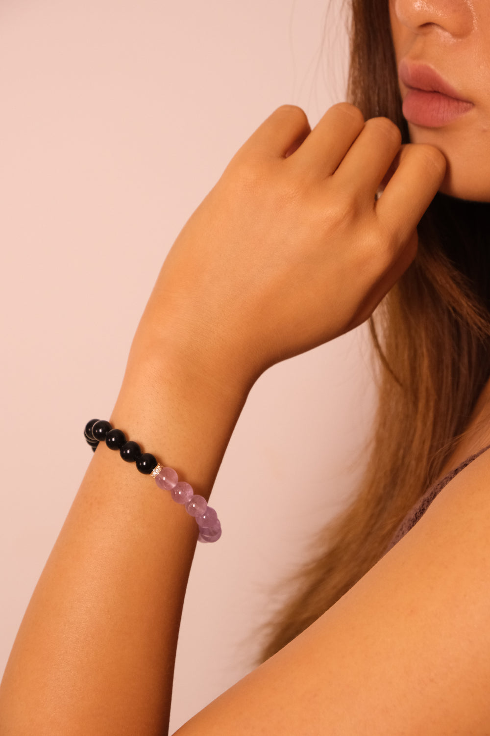 Close-up of a woman wearing the Tibetan Dual Energy Bracelet made of black obsidian and purple amethyst beads, photographed against a light pink background.