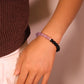 Close-up of a woman wearing the Tibetan Dual Energy Bracelet made of black obsidian and purple amethyst beads, photographed against a light pink background.