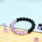 Black beaded bracelet with pink and purple beads on a light blue fabric background