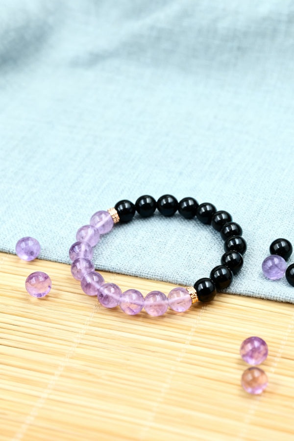 Black beaded bracelet with pink and purple beads on a light blue fabric background