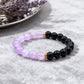 Two beaded bracelets, one purple and one black, on a gray surface with lavender flowers.