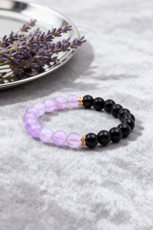 Two beaded bracelets, one purple and one black, on a gray surface with lavender flowers.