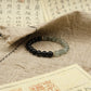Black and green Tibetan Dual Energy beaded bracelet on a textured surface with classical Chinese text