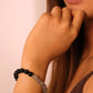 Close-up of a person wearing a Tibetan Dua _Energy beaded bracelet on a plain background