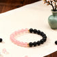 Two beaded bracelets, one pink and one black, on a wooden surface with a vase of flowers in the background.