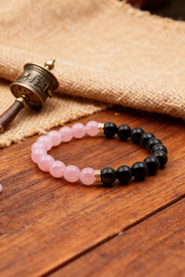 Bracelet with pink and black beads on a wooden surface with a small prayer wheel.