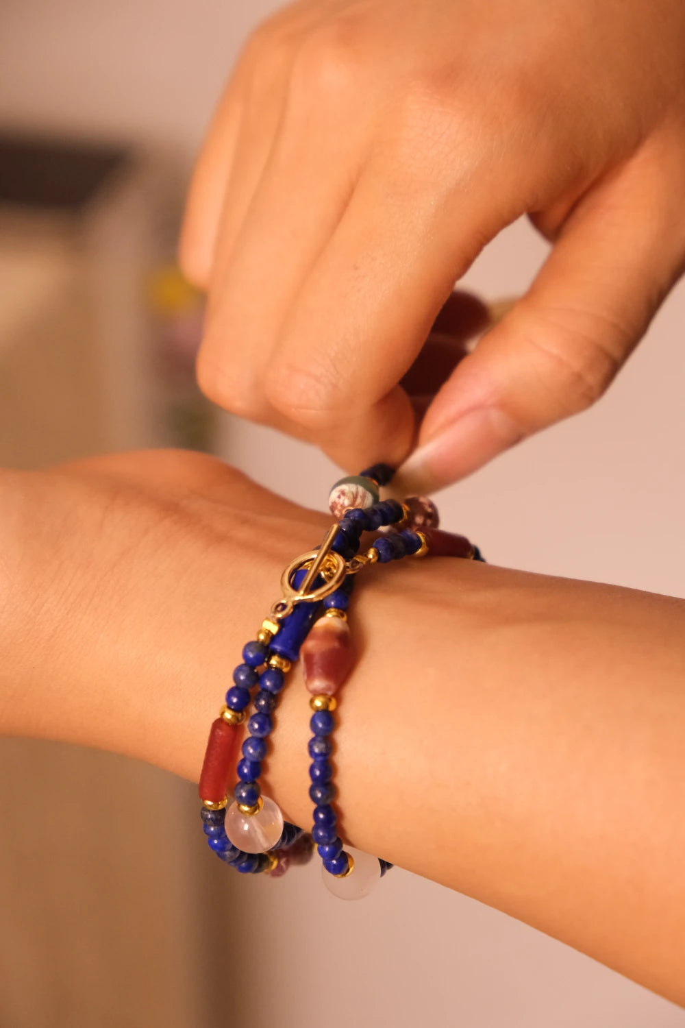 Close-up of a hand wearing aLapis Lazuli & Amber bracelet on a blurred background
