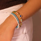 Close-up of a wrist wearing a bracelet featuring multiple strands with elements like pearls, turquoise, and ornate decorative beads on a neutral background