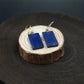 Blue rectangular earrings on a wooden stand with a dark background, Tibetan Feng Shui Crystal Earrings – Lapis Lazuli for Protection, Purification & Well-Being