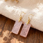 Pink crystal earrings with gold hooks on a wooden surface with beige fabric in the background