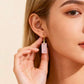 Close-up of a woman wearing a pink crystal earring against a beige background