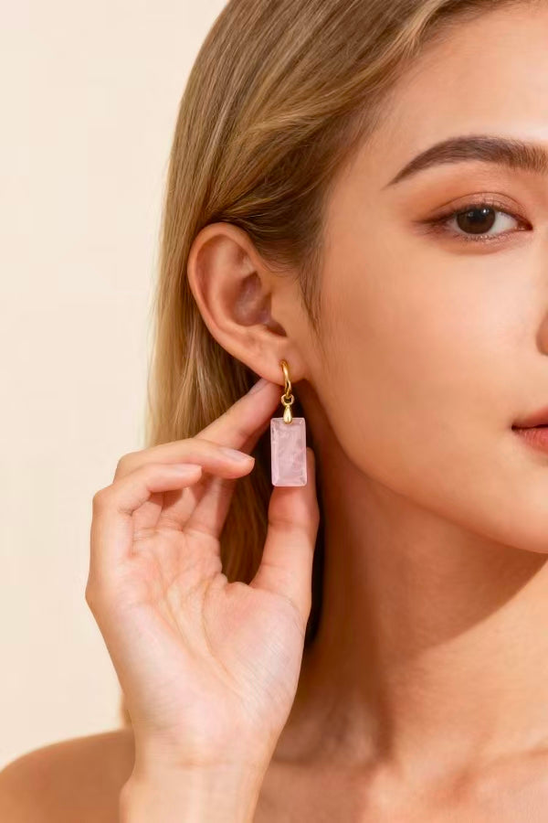 Close-up of a woman wearing a pink crystal earring against a beige background
