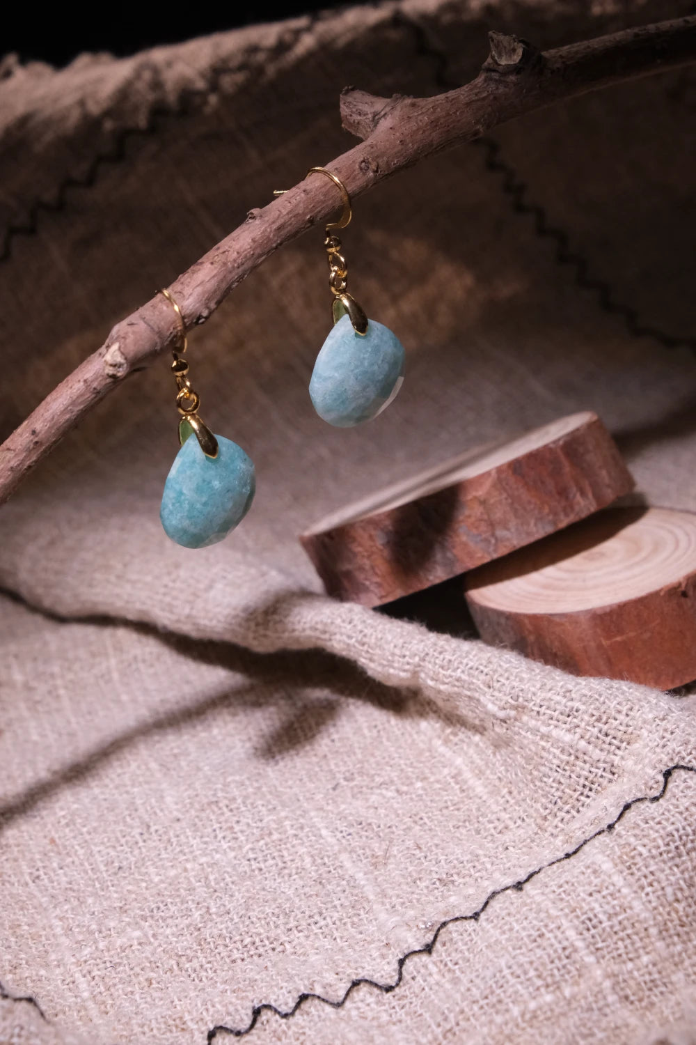 Confidence & Renewal – Tibetan Amazonite Earrings hanging from a branch on a textured fabric background