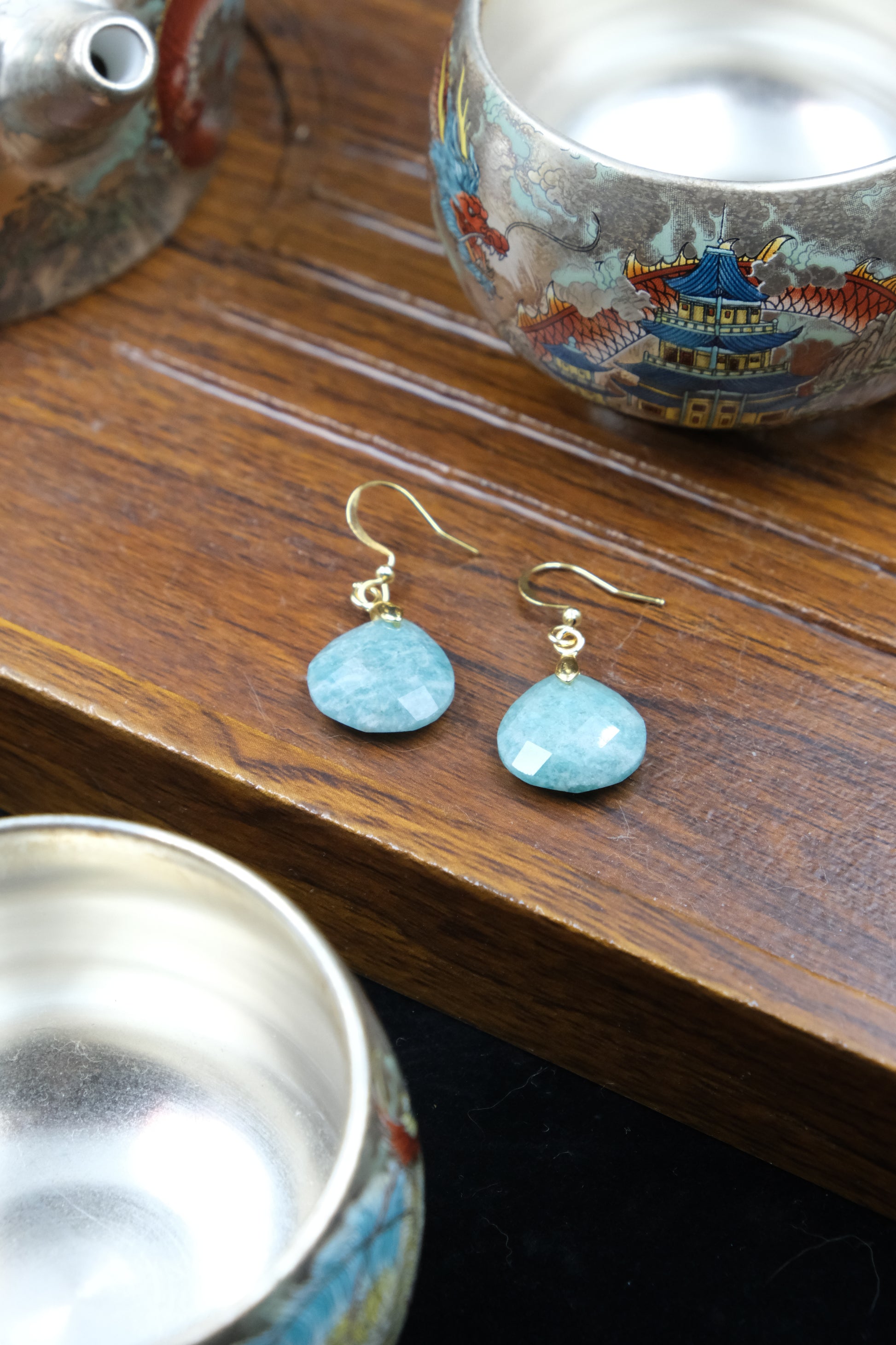 Confidence & Renewal Tibetan Amazonite Earrings on a wooden surface with decorative bowls in the background