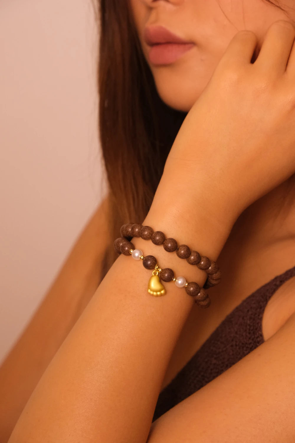 Close-up of a person wearing a Natural Aromatherapy Beads with Pearls & Golden Foot Charm for Protection, Balance & Inner Peace, with a bell charm on a neutral background