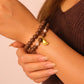 Close-up of a wrist wearing a Peace & Harmony – Tibetan Pearl Five Elements Bracelet with a gold charm against a neutral background.